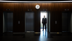 Businessman standing in lit elevator doorway office dark