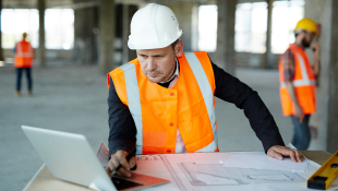 Construction worker looking at laptop and plans