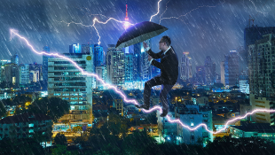 Businessman with umbrella battling thunderstorm with highrises behind him