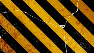 Cracks running through caution black and yellow striped sign